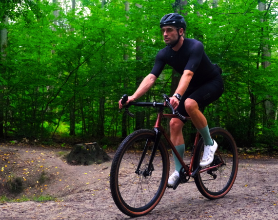 Kolarz jedzie na rowerze marki Antymateria typu gravel przez las