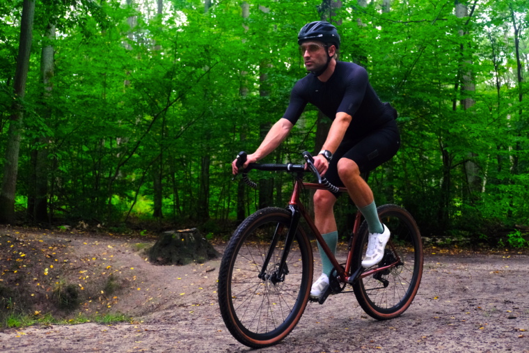 Kolarz jedzie na rowerze marki Antymateria typu gravel przez las